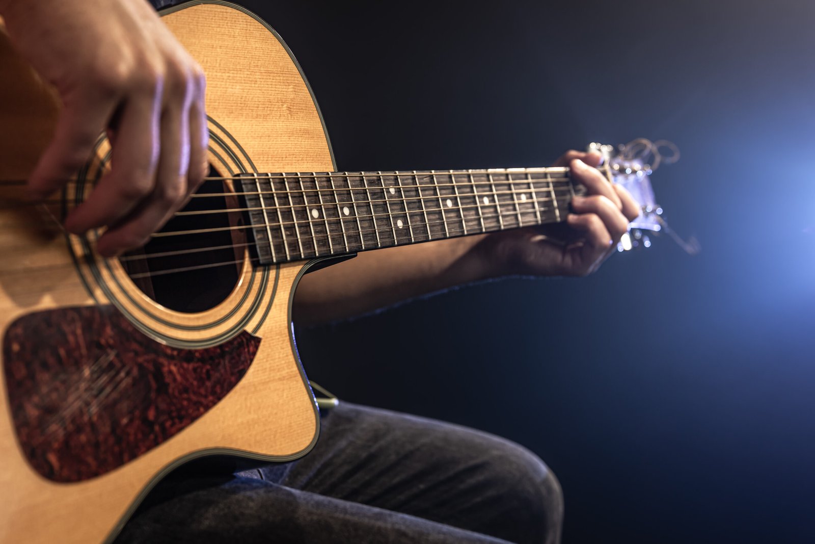 close up man playing acoustic guitar dark with stage lighting scaled